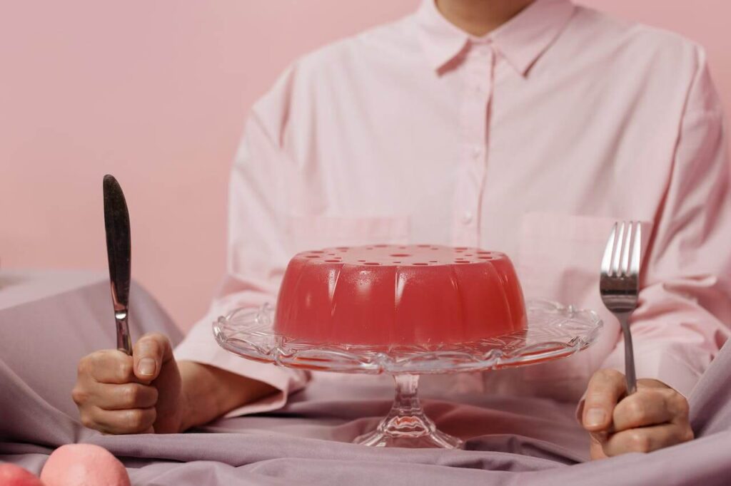Woman standing with forks in front of a large strawberry gelatin, a wisdom tooth extraction-friendly dessert