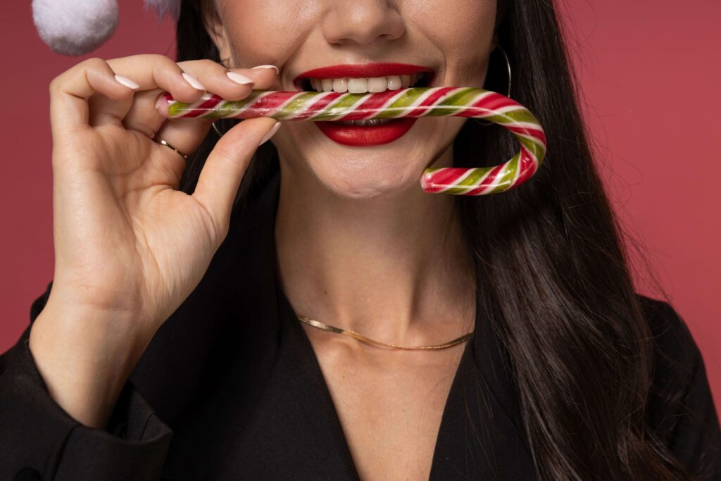 A lovely girl with a candy cane held between her teeth.