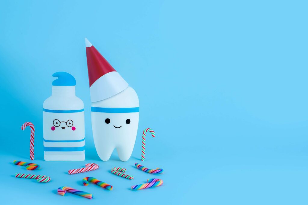 A tooth wearing a New Year's hat next to toothpaste and surrounded by candy canes.