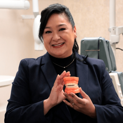 Dra. Cirenia Aparicio holding a dentures in a dental clinic with background brown color