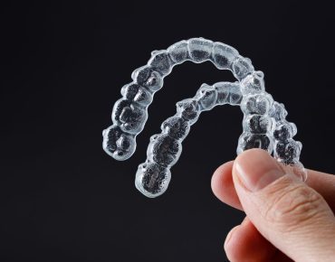 hands holding a pair of invisalign with a background black